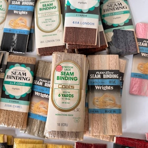 May include: A collection of vintage seam binding rolls in various colors, including black, brown, beige, and pink. The packaging features the brand names "Wrights", "Flexi-Lace", and "J. & P. Coats", with text indicating the length and material (nylon).