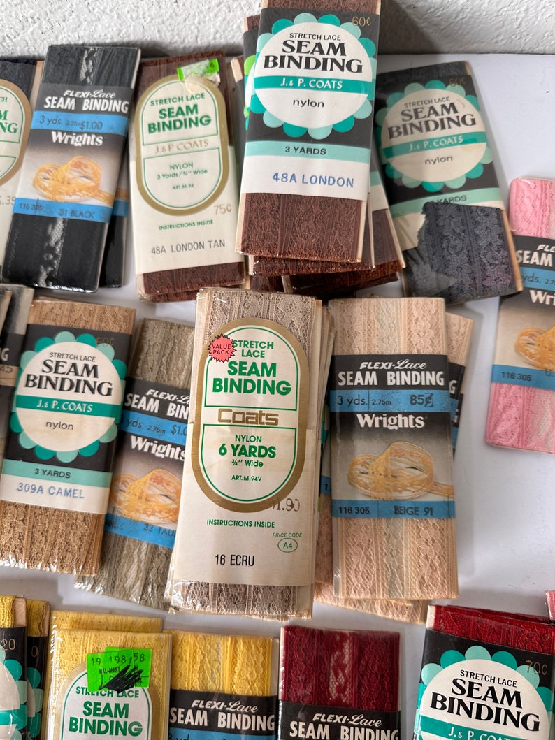 May include: A collection of vintage seam binding rolls in various colors, including black, brown, beige, and pink. The packaging features the brand names "Wrights", "Flexi-Lace", and "J. & P. Coats", with text indicating the length and material (nylon).