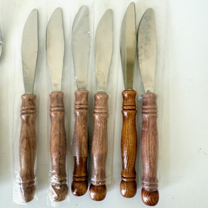 K&ouml;nnte beinhalten: Set mit sechs Edelstahl-Buttermessern mit Holzgriffen. Die Griffe sind in warmen Braunt&ouml;nen gehalten und haben ein dekoratives, gedrehtes Design. Die Messer sind einzeln in Klarsichtfolie verpackt.