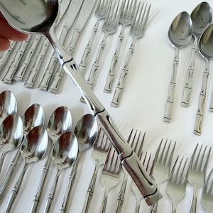 Könnte beinhalten: Eine Sammlung von Edelstahlbesteck mit Bambus-Design. Das Set umfasst Löffel, Gabeln und Messer, die alle auf einer weißen Oberfläche angeordnet sind. Das Besteck hat eine glänzende, reflektierende Oberfläche.