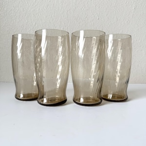 May include: A set of four tall drinking glasses made of translucent smoke-colored glass. Each glass features a distinct vertical swirl pattern that creates a rippled texture along the exterior surface, with a slightly flared rim and a weighted base.