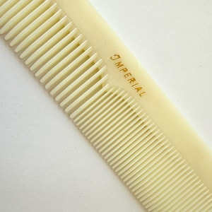 May include: Ivory-colored comb with fine and wide teeth. The comb has the word "IMPERIAL" printed in gold. The comb is made of a smooth, solid material.