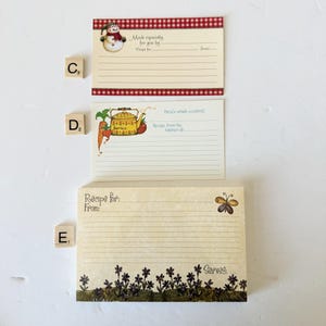 May include: Three recipe cards with decorative borders and illustrations. One card features a snowman, another a teapot with vegetables, and the third a butterfly. Each card has lines for recipe details.