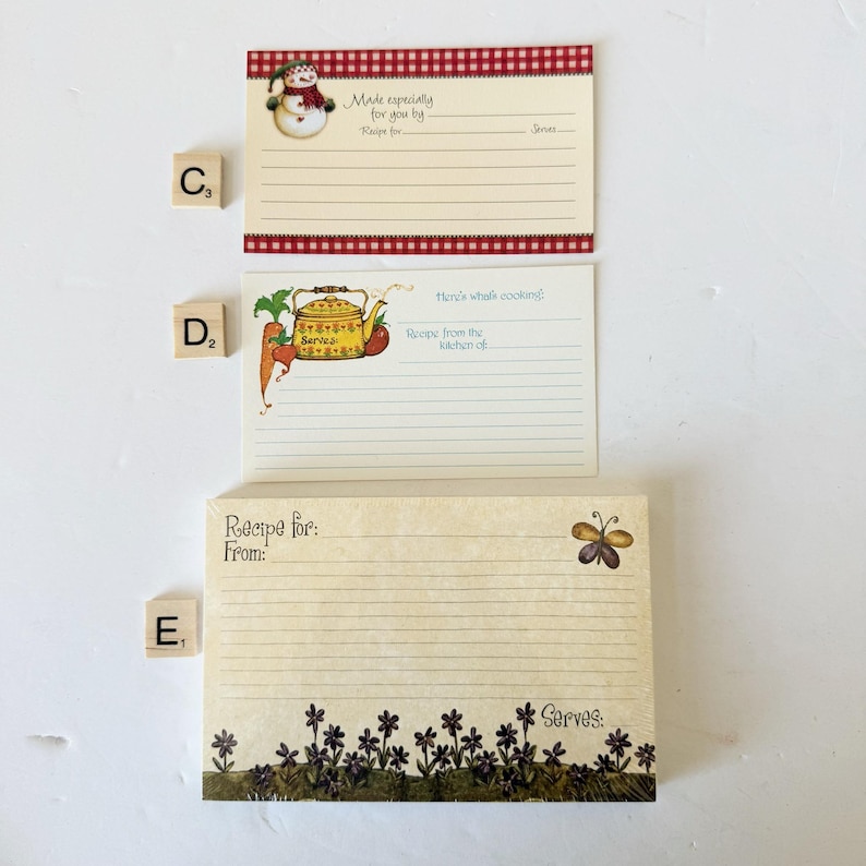 May include: Three recipe cards with decorative borders and illustrations. One card features a snowman, another a teapot with vegetables, and the third a butterfly. Each card has lines for recipe details.