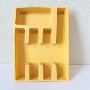 May include: A rectangular yellow plastic cutlery tray featuring a single horizontal compartment at the top and five vertical dividers below, creating six distinct sections for organizing kitchen utensils and flatware in a drawer.