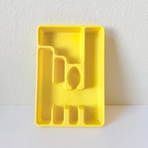 Puede incluir: Una bandeja de cubiertos de plástico amarillo brillante con múltiples compartimentos para organizar la cubertería. La bandeja tiene forma rectangular con varias ranuras y divisores para guardar tenedores, cuchillos y cucharas. Diseñada para un cajón de cocina.