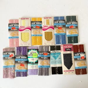 May include: A collection of vintage Flexi-Lace seam binding in various colors, including pink, yellow, gold, blue, and black. Each package contains 3 yards of binding and features the Wrights and Talon brands. Ideal for sewing and craft projects.