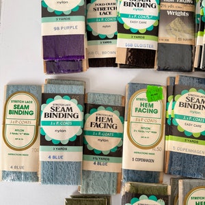 May include: A collection of vintage stretch lace seam binding and hem facing in various colors, including purple, brown, and blue. The packages are labeled with the brand J. & P. Coats and include details like yardage and color names.