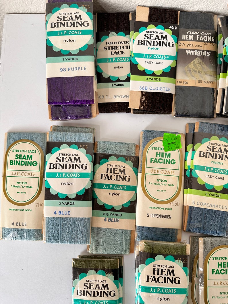 May include: A collection of vintage stretch lace seam binding and hem facing in various colors, including purple, brown, and blue. The packages are labeled with the brand J. & P. Coats and include details like yardage and color names.