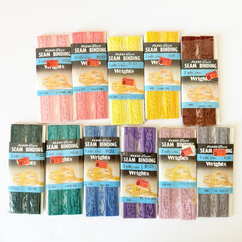 May include: A collection of Flexi-Lace seam binding in various colors, including pink, yellow, teal, blue, purple, and gray. Each package contains 3 yards of lace and features the "Wrights" brand. Some packages have clearance stickers.