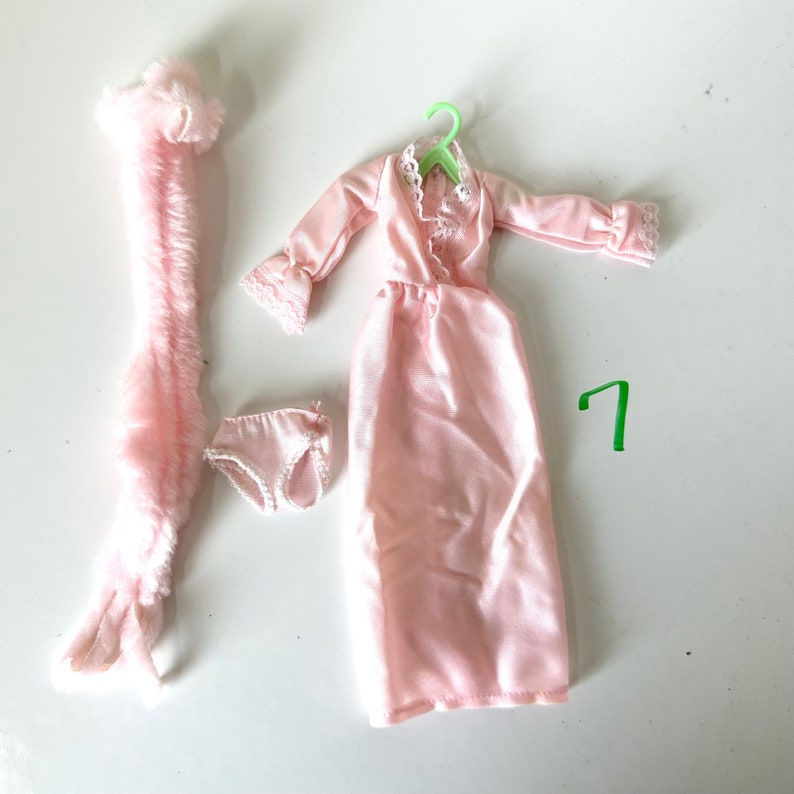 Op de afbeelding: Een roze satijnen nachtjapon met kantversiering, een roze pluche badjas en een paar roze ondergoed. De nachtjapon hangt aan een groene plastic hanger.