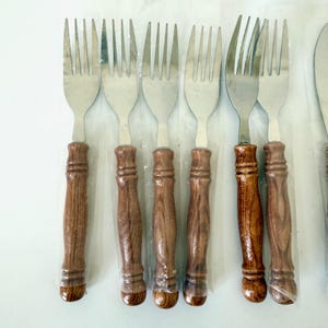 K&ouml;nnte beinhalten: Ein Set aus Edelstahlgabeln mit Holzgriffen. Die Griffe sind mittelbraun mit einem Holzmaserungsmuster. Die Gabeln sind in klarem Kunststoff verpackt.