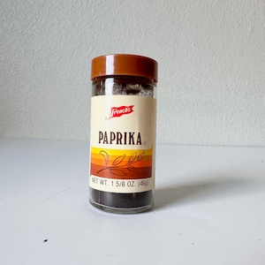 May include: A clear glass jar of French's paprika with a brown lid. The label features the word "PAPRIKA" in bold letters, with a colorful stripe design and the text "NET WT. 1 5/8 OZ. (46g)".