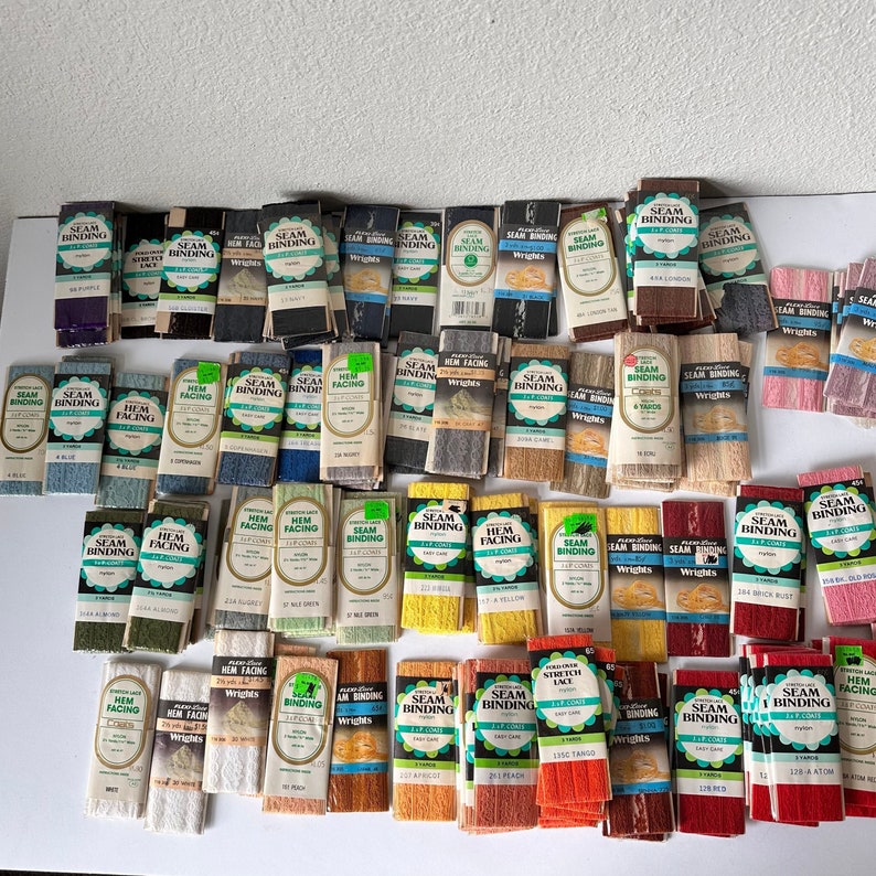 May include: A collection of various colors of seam binding and hem facing, neatly arranged. The packages display the "Wrights" brand and include colors like purple, blue, and yellow. The image showcases a variety of sewing supplies.