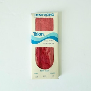 May include: A package of red stretch lace hem facing by Talon. The package has the text "HEM FACING" and "stretch lace 1 1/4" wide". The package also has the text "100% nylon", "ITEM 216", and "COLOR 415".