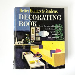 Puede incluir: Libro de decoración vintage "Better Homes & Gardens" con una portada negra y texto amarillo. La portada presenta una ilustración de salón moderno de mediados de siglo con un sofá amarillo, una mesa de centro blanca y obras de arte enmarcadas. El libro promete más de 300 ilustraciones a color.