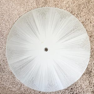 May include: A circular, frosted glass light fixture shade featuring a radiating sunburst pattern of thin, etched white lines that extend from a central circular opening outward toward the smooth, rounded edges of the glass disc.