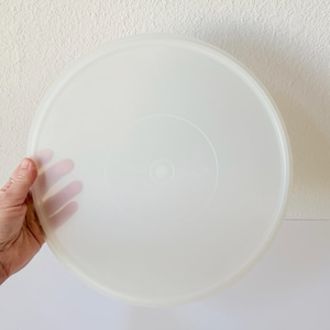 Puede incluir: Una tapa redonda de plástico blanquecino. La tapa es translúcida, con una superficie ligeramente texturizada. Tiene un borde elevado y una hendidura circular central. La tapa está diseñada para un recipiente.