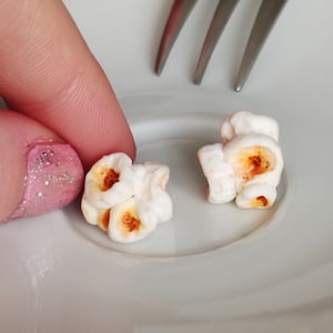 Peut inclure: Deux petits morceaux de popcorn blancs avec des grains bruns sur une assiette blanche.