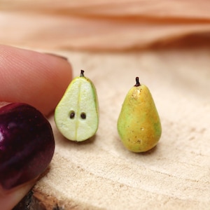 May include: Two miniature pear figurines, one cut in half to show the inside, the other whole. The pears are green and yellow with brown stems. The pears are sitting on a wooden surface.