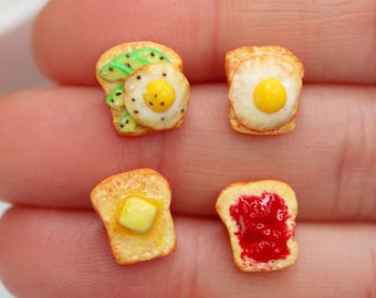 Puede incluir: Miniaturas de comida: tostadas con aguacate y huevo frito, tostadas con huevo frito, tostadas con mantequilla y tostadas con mermelada. Las tostadas son doradas y los ingredientes son coloridos y detallados.