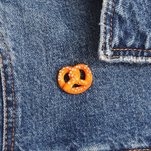 Op de afbeelding: Een kleine oranje pretzel met witte sprinkels op een blauwe denim achtergrond.