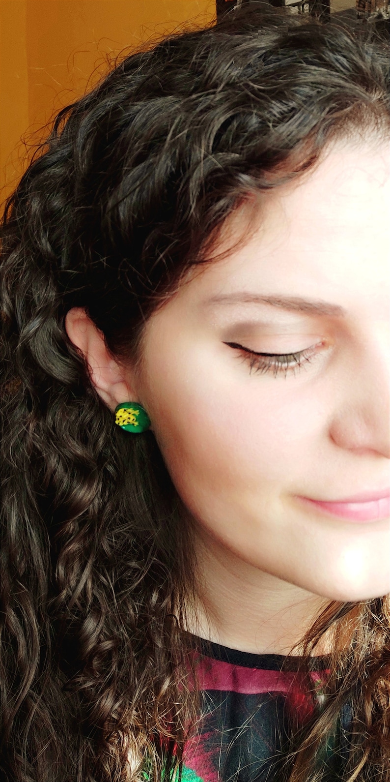 Puede incluir: Una mujer con el pelo largo y rizado casta&ntilde;o que lleva pendientes en forma de pi&ntilde;a verde y amarilla.