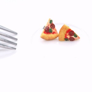 May include: Two miniature pizza slices with pepperoni, basil, and red sauce on a white plate. A silver fork is in the upper left corner. The pizza crust is golden brown.