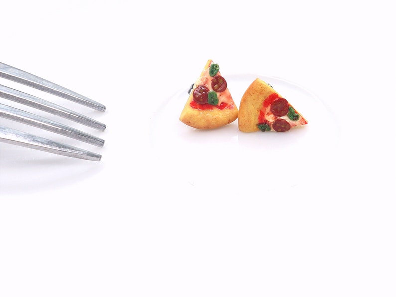 May include: Two miniature pizza slices with pepperoni, basil, and red sauce on a white plate. A silver fork is in the upper left corner. The pizza crust is golden brown.
