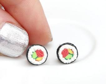 May include: A pair of sushi earrings, each featuring a small, detailed replica of a maki roll with red, green, and white filling. The earrings are on a white surface.