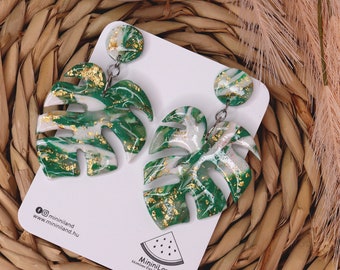 May include: A pair of green and white monstera leaf earrings with gold flecks. The earrings are on a white card with the text "Miniiniland" and a watermelon logo.