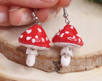 Op de afbeelding: Een paar rode en witte paddenstoel oorbellen met zilveren haakjes. De paddenstoelen hebben witte stippen en een getextureerde witte steel.