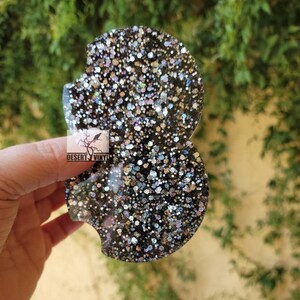 Puede incluir: Dos posavasos de resina negra con un acabado brillante. La purpurina es una mezcla de colores plata, negro e iridiscente.