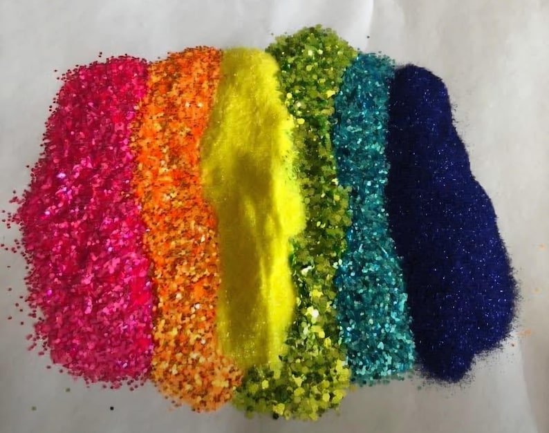Puede incluir: Una vibrante exhibici&oacute;n de purpurina colorida en un arreglo de arco&iacute;ris. Los colores incluyen rosa, naranja, amarillo, verde, turquesa y azul. La purpurina se extiende en montones separados, creando una presentaci&oacute;n visualmente atractiva y festiva.