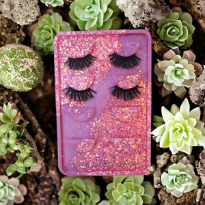 May include: A pink and purple resin tray with glitter embedded in the resin. The tray has four compartments, each containing a set of false eyelashes.