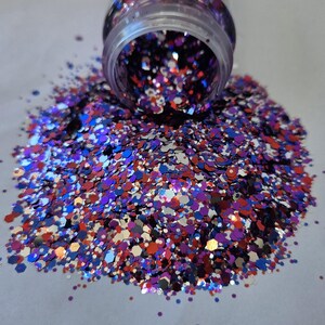 May include: A clear jar tipped over, spilling a vibrant mix of glitter. The glitter is a blend of red, blue, silver, and purple, with a hexagonal shape. The glitter is scattered across a white surface.