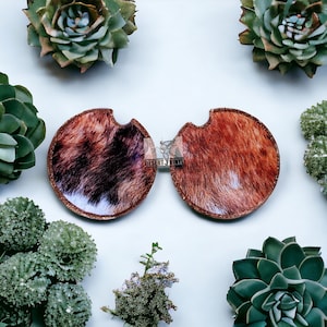 May include: Two brown and white cowhide print car coasters with a gold glitter edge.