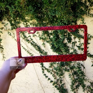May include: Red glitter license plate frame. The frame is made of metal and has a shiny, sparkly finish.