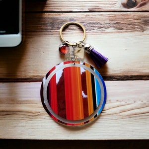 May include: A round, colorful key chain with a striped design in shades of red, orange, and blue. The key chain has a silver ring and a purple tassel.