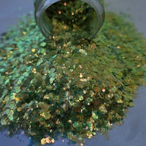May include: A clear glass jar tipped over, spilling a pile of iridescent glitter. The glitter is a mix of green, gold, and iridescent colors, creating a shimmering effect. The glitter is in various shapes and sizes, reflecting light. The image is a close-up, highlighting the texture and sparkle.