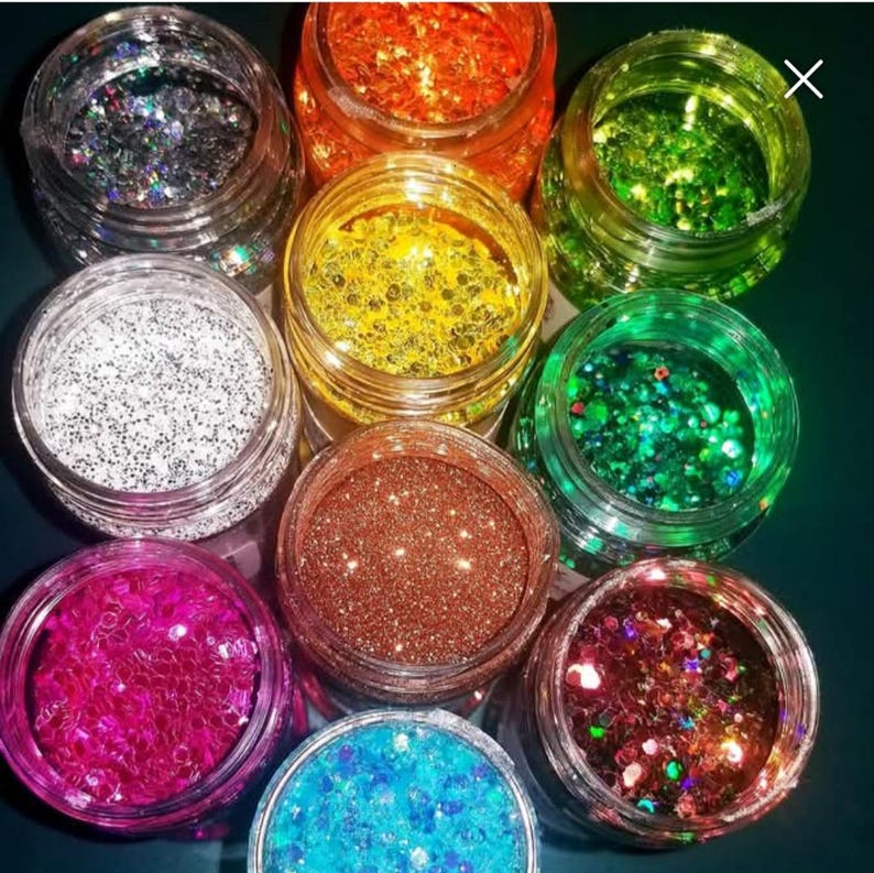 Puede incluir: Una colecci&oacute;n de peque&ntilde;os frascos transparentes llenos de purpurina de varios colores. Los colores de la purpurina incluyen plata, naranja, amarillo, verde, blanco, marr&oacute;n, rosa, azul y una mezcla de rojo y marr&oacute;n. Los frascos est&aacute;n dispuestos en un patr&oacute;n circular.