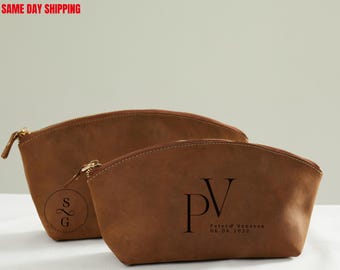 May include: Two brown leather cosmetic bags with gold zips. One bag has the initials "PV" and the date "06.06.2022" printed on it. The other bag has the initials "SG" printed on it. The bags are on a light background.