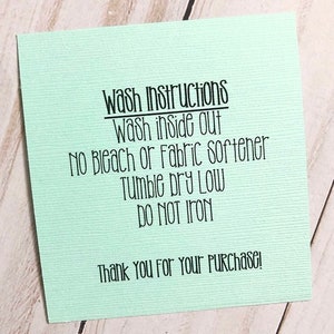 May include: A pale green card with black text detailing wash instructions, including "Wash inside out" and "Do not iron". The card also includes the text "Thank You For Your Purchase!"