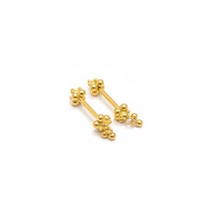 May include: A pair of gold-toned barbell body jewelry pieces. Each barbell features a straight post with a cluster of small, round spheres at both ends, creating a textured, beaded appearance on the decorative terminals of the jewelry.