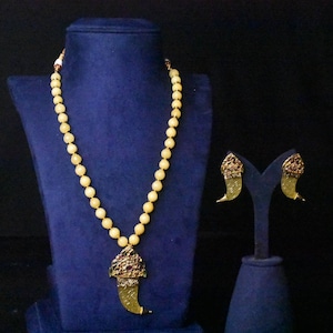 May include: A gold necklace with a claw pendant and matching earrings. The necklace is made of cream-colored beads and the pendant and earrings are decorated with red and gold accents.