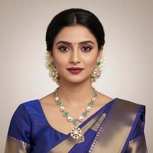 May include: A gold necklace featuring round green stones and a central teardrop pendant with a clear stone, paired with matching teardrop-shaped earrings. The jewelry set is worn with a deep blue garment featuring a wide gold metallic border.