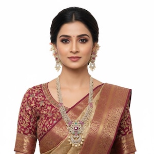 May include: A long necklace and matching drop earrings set featuring intricate silver-toned metalwork, embedded with small white stones, pink rectangular center stones, and small green accents, worn with a maroon and gold patterned blouse.