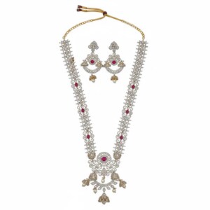 May include: A long necklace and matching earrings set featuring silver-toned metal, clear white stones, and oval-shaped pink stones. The necklace has a central pendant with dangling bell-shaped charms and a gold-toned adjustable cord closure.