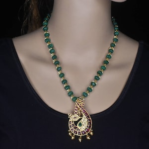 Puede incluir: Un collar de cuentas verdes con un colgante de pavo real dorado. El colgante está decorado con piedras rojas y blancas.