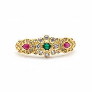 May include: A gold ring featuring a central round green gemstone surrounded by small clear round stones. Two pear-shaped pink gemstones are set on either side, with additional clear round stones embedded in the intricate gold metal band design.